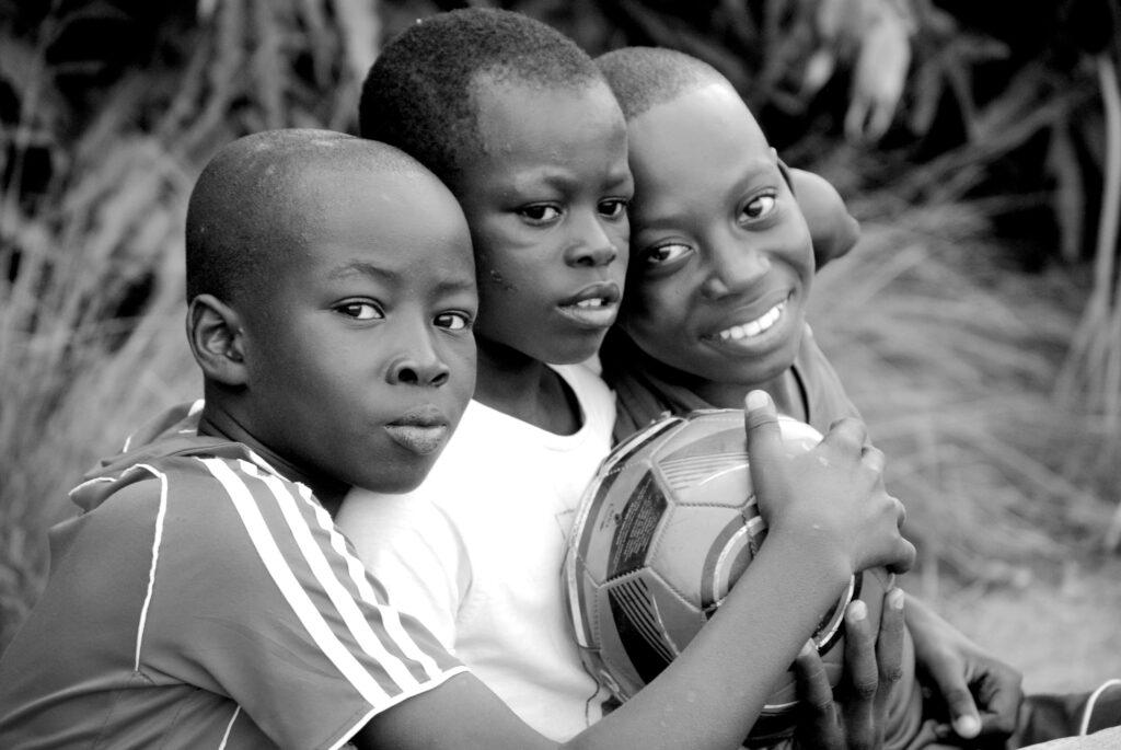 Three African boys happily embracing a soccer ball outdoors in Togo.